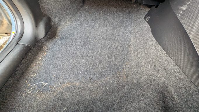 Dirty rear footwell carpet of a Honda Jazz in Market Deeping before detailing, showing dust and debris on the surface.