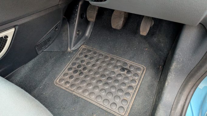 Ford KA driver’s footwell in Yaxley, Peterborough before interior detailing, with dirt and debris visible on mats and carpet.