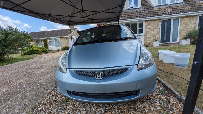 Dirty blue Honda Jazz parked on a driveway in Market Deeping, Lincolnshire showing road grime and dull paintwork on the front.