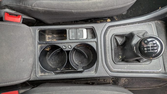 Dirty VW Touran centre console in St Ives, Cambridgeshire before interior detailing, with dust, crumbs and debris visible in cup holders.