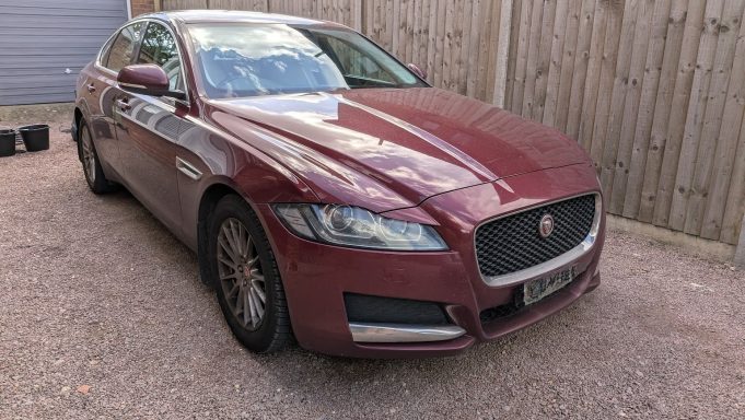 Front angle of a maroon Jaguar XF in Cambridge before detailing, with dull paintwork and dirt on the wheels and lower panels.