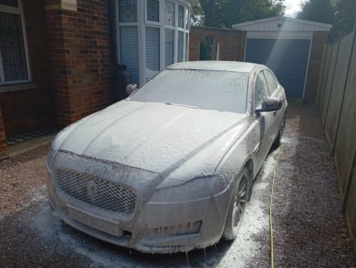 Jaguar XF in Cambridge covered in thick snow foam during the detailing process.
