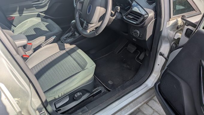 Driver’s side interior of a Ford Fiesta in Barnack, Peterborough before detailing, showing dirt on the floor mats and dust on the dashboard.