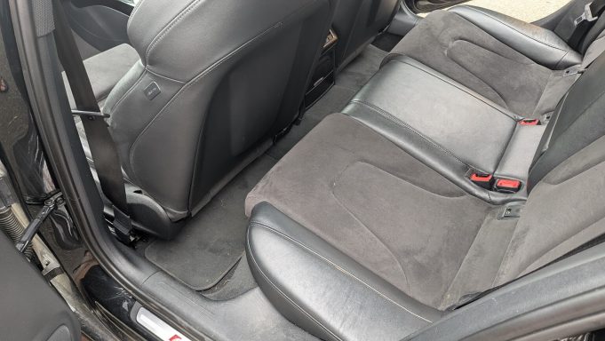 Rear seats of black Audi S4 in Huntingdon before interior detailing, showing dust and light debris on upholstery and carpets.
