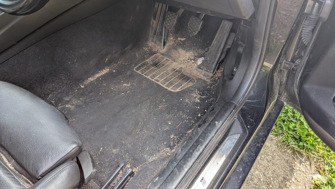 Dirty driver’s footwell of a BMW 3 Series in Stilton, Peterborough before deep interior detail, showing heavy dust and debris.