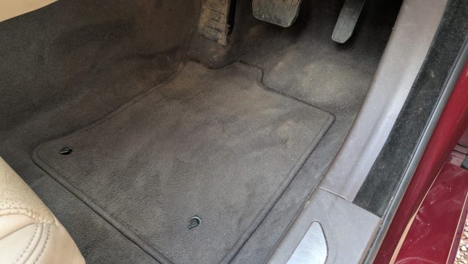 Driver’s footwell of a Jaguar XF in Cambridge before detailing, with dirt and dust visible on the carpet mats.