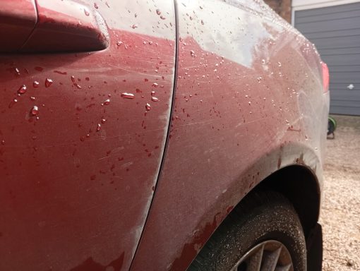 Close-up of a maroon Jaguar XF in Cambridge before detailing, showing dull paintwork and dirt near the wheel arch.
